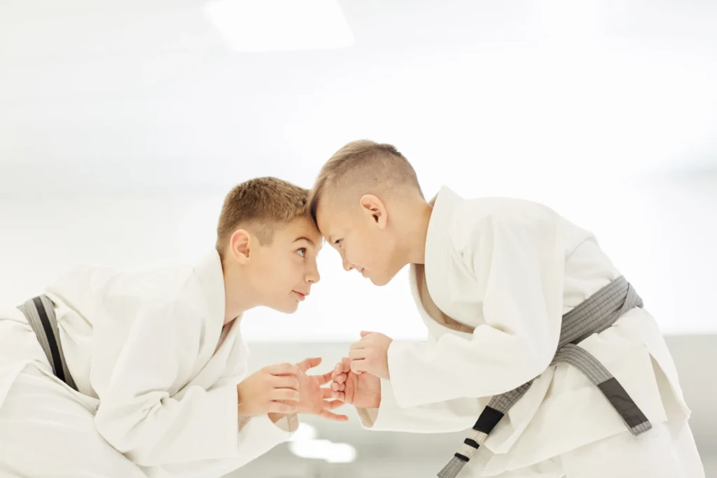 Duas crianças praticando judô, vestidas com kimono, enfrentando-se de cabeça baixa em uma competição de artes marciais, demonstrando força e disciplina.