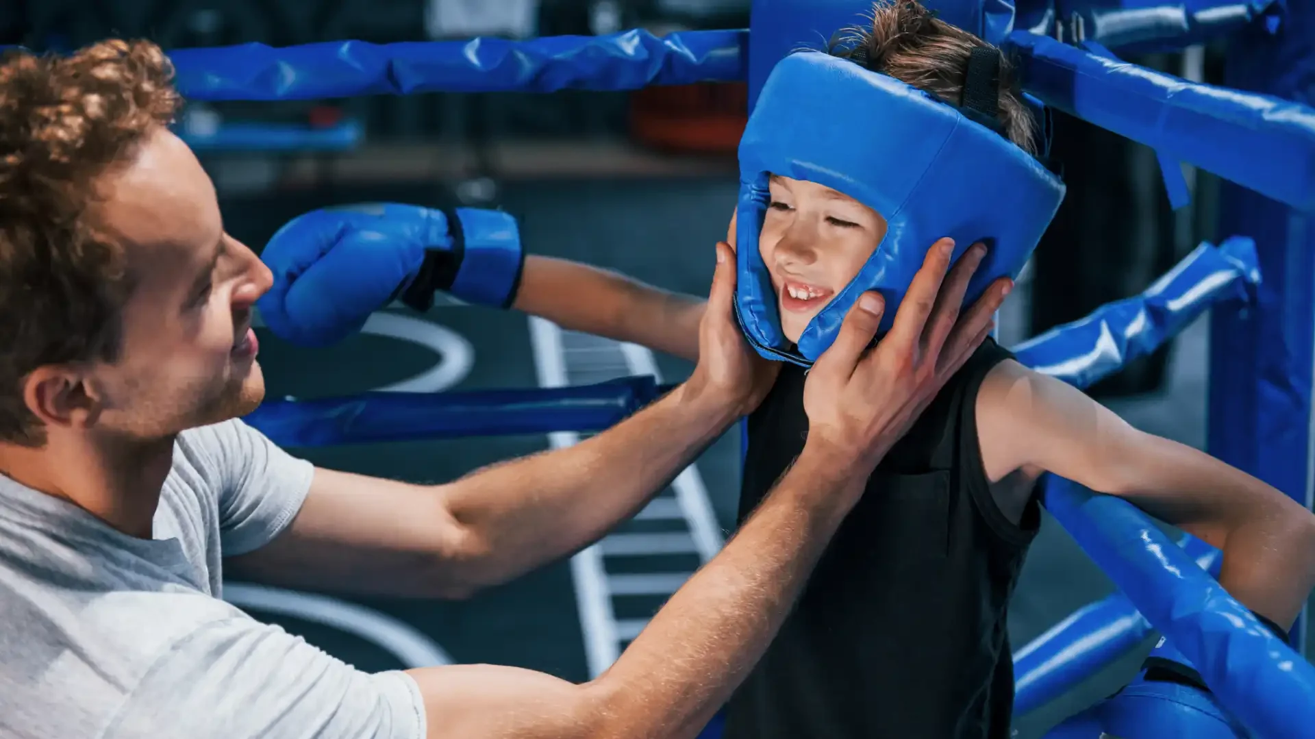 Treinador ajudando criança a treinar boxe no ringue, em ambiente de academia. Cena de incentivo e aprendizagem de artes marciais para crianças.