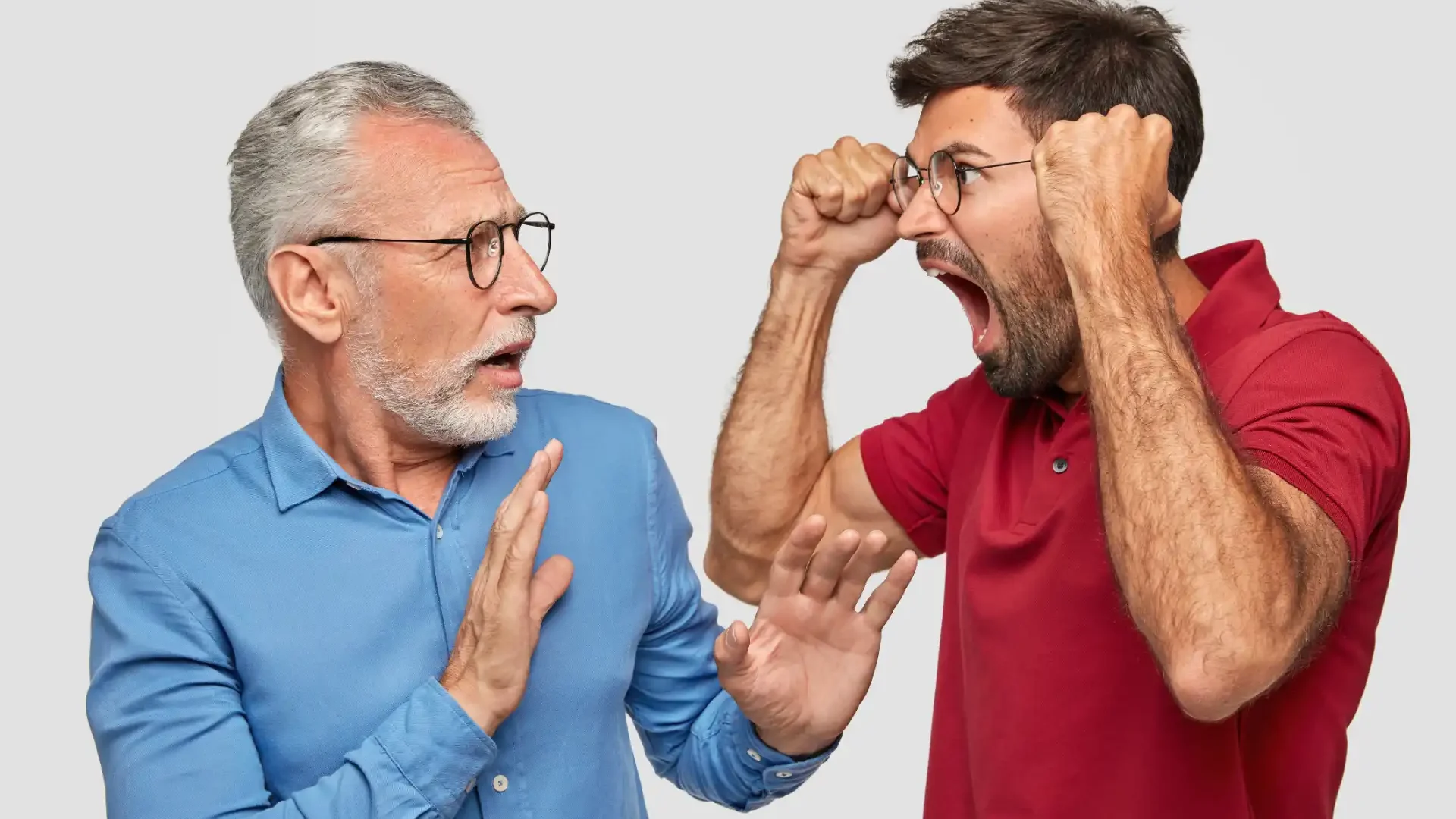 Homem mais velho tentando acalmar homem mais jovem que está bravo e gritando, ambos usando óculos e camisetas de cor azul e vermelha.