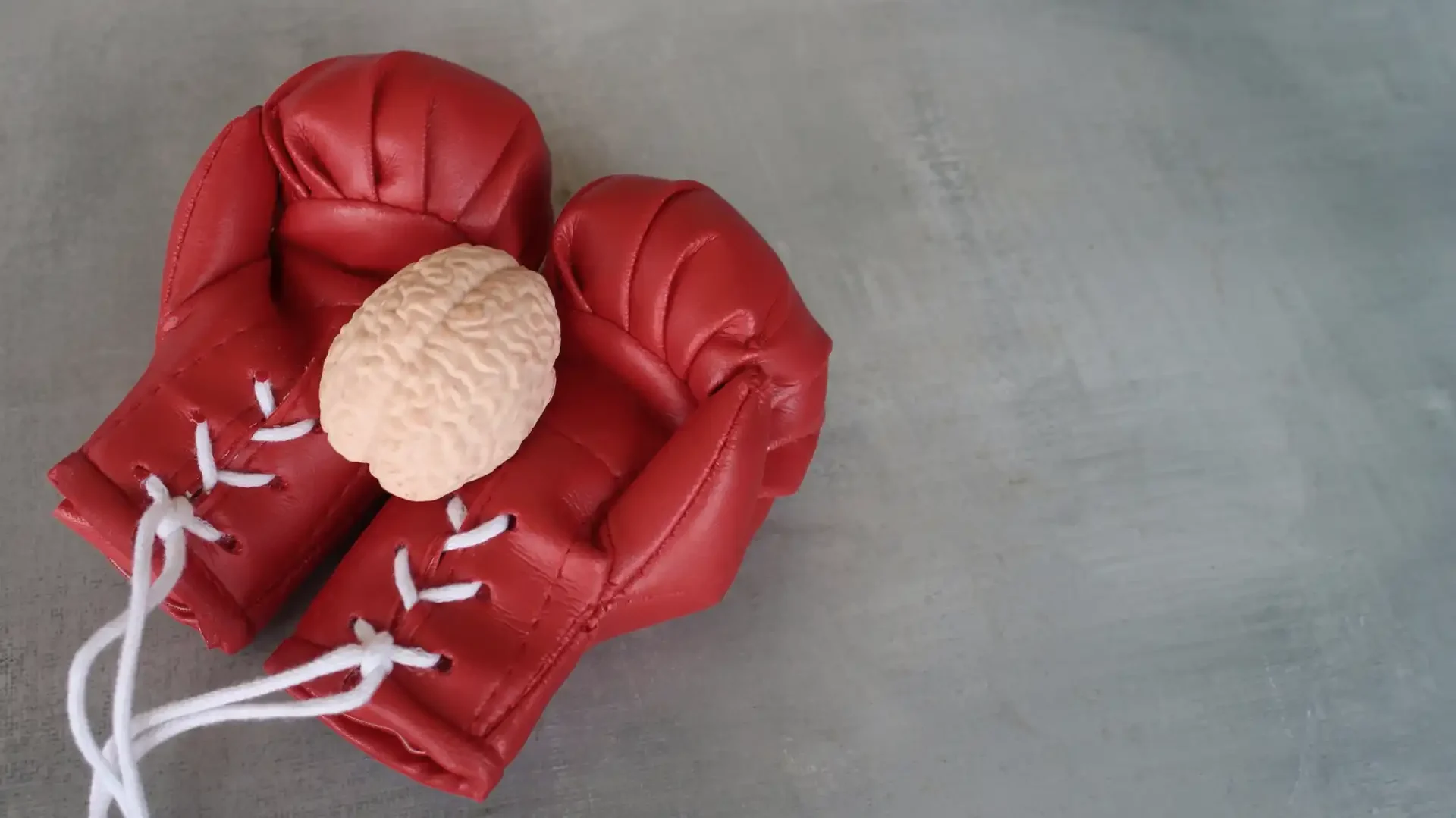 Imagem de uma dupla de luvas de boxe vermelhas segurando um cérebro, simbolizando a força mental na prática do boxe. Ideal para conteúdo sobre saúde mental, esportes de combate e bem-estar.
