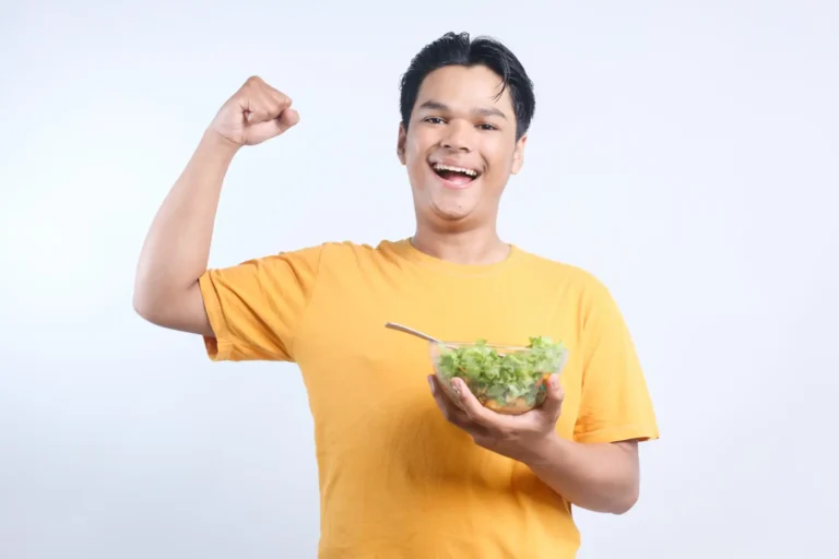 Homem feliz segurando uma tigela de salada em um fundo branco, celebrando uma alimentação saudável e bem-estar.