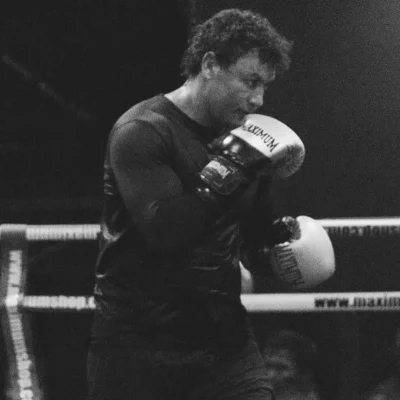 Imagem em preto e branco do Popo boxeador treinando na ringue, concentrado enquanto segura suas luvas de boxe, com foco na preparação esportiva.