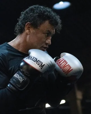 Popo treinando boxe com luvas da marca Maximum, focado e preparado para o combate, em ambiente de treino com iluminação escura.