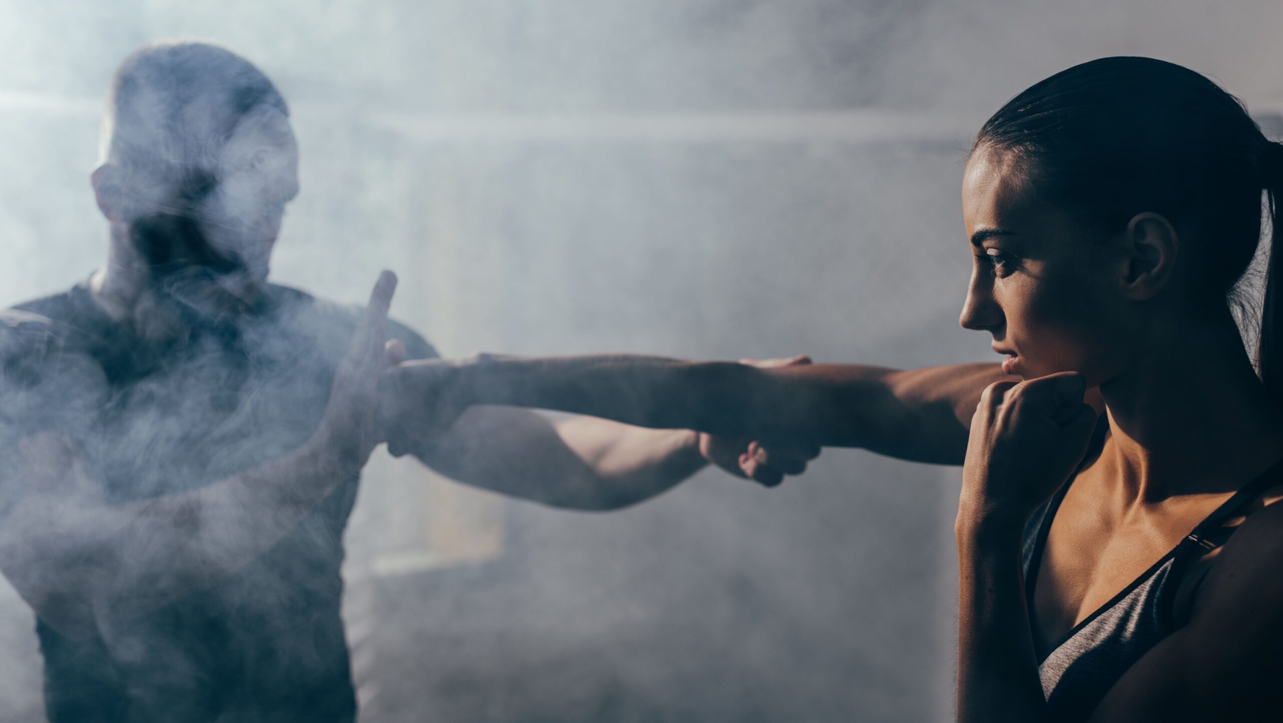 Mulher treinando artes marciais, praticando socos na frente de um adversário oculto, em ambiente de academia de luta, foco na preparação física e resistência.