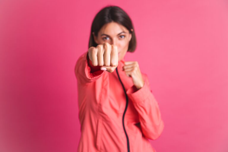 Mulher vestida de rosa fazendo um golpe de lutadora, simbolizando força, resistência e empoderamento feminino.