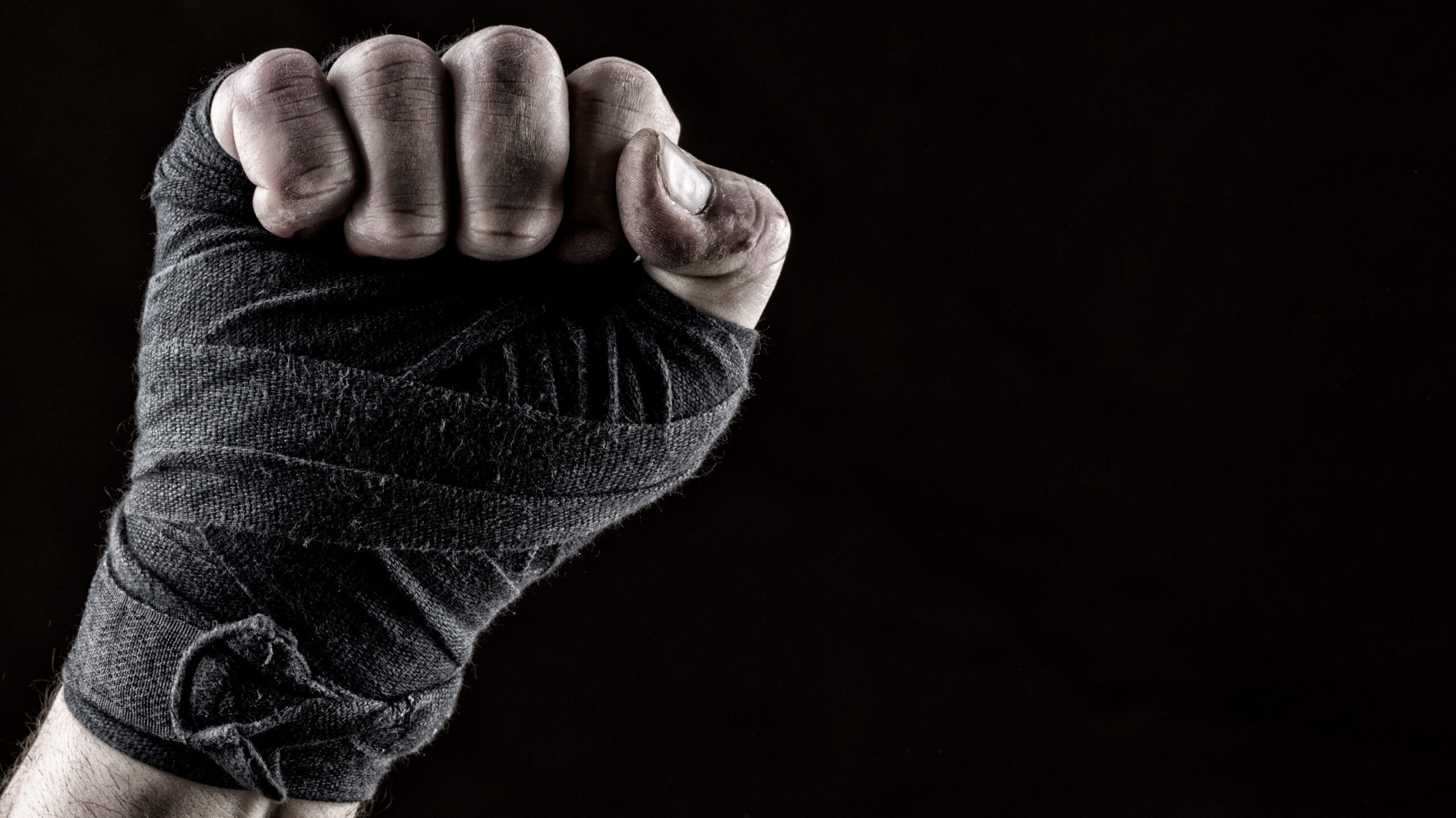 Mão fechada em punho, envolta em faixa de proteção contra um fundo preto.