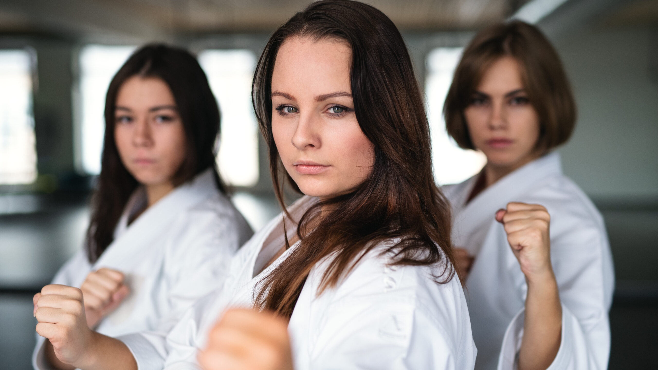 Três mulheres praticando karatê em um dojo, demonstrando força, determinação e empoderamento feminino.