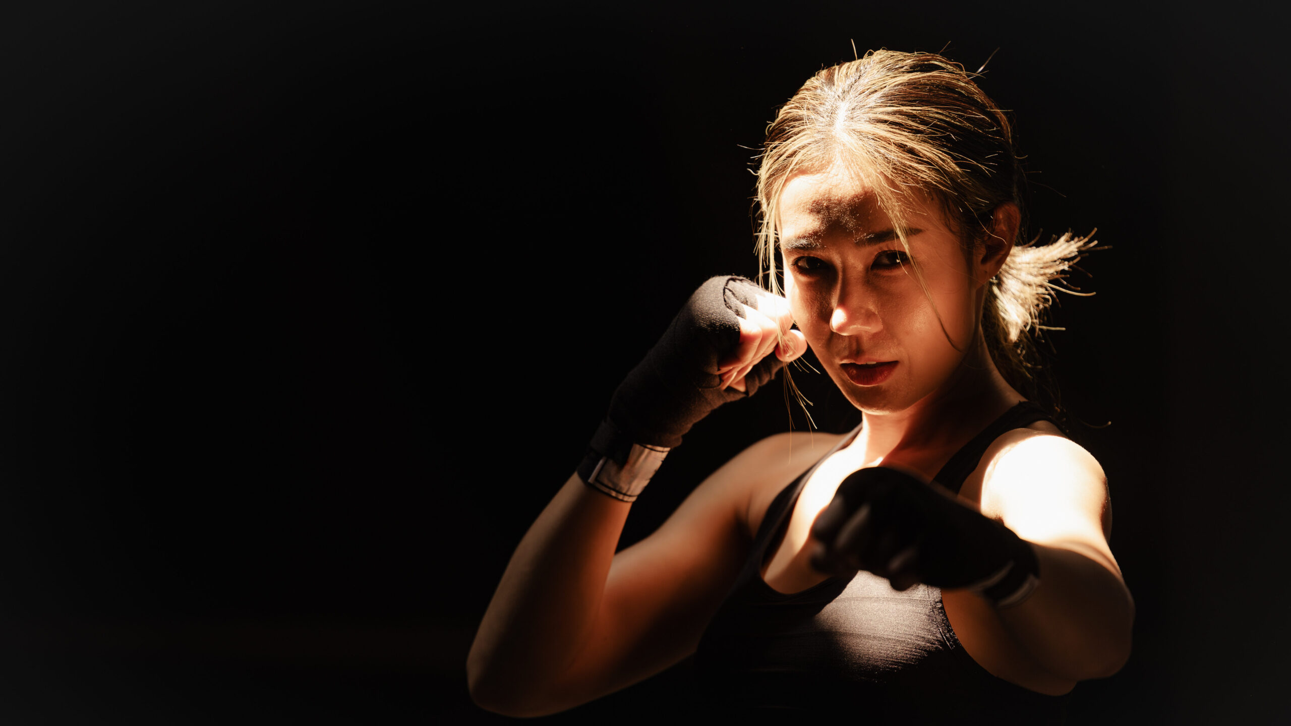 Mulher lutadora de muay thai ou boxe, vestida com roupas esportivas e luvas de proteção, posando em uma luta ou treino, com expressão de determinação.