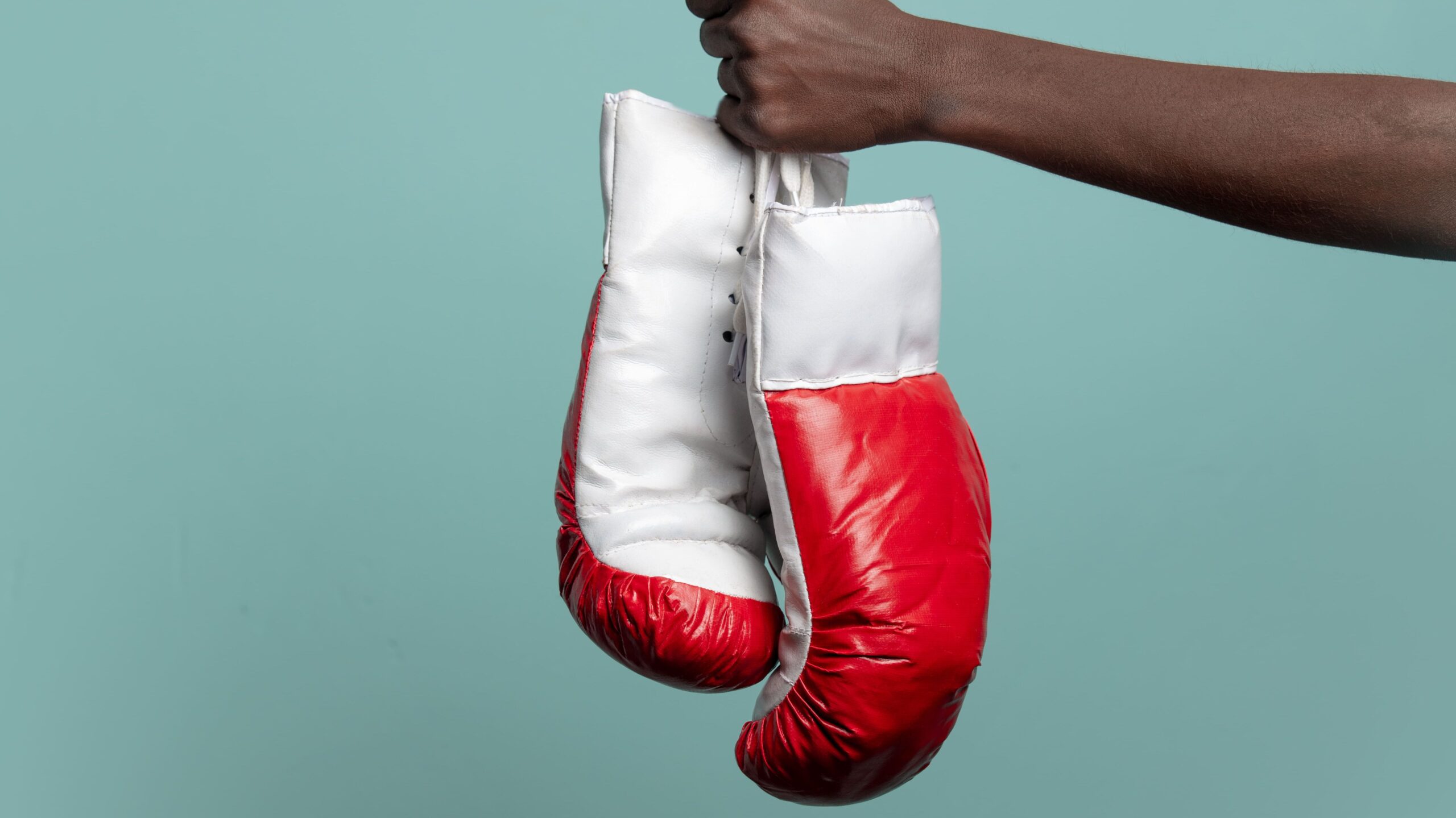 Soco de boxe vermelho e branco sendo segurado por uma mão contra fundo azul claro, simbolizando esporte de luta e treinamento.