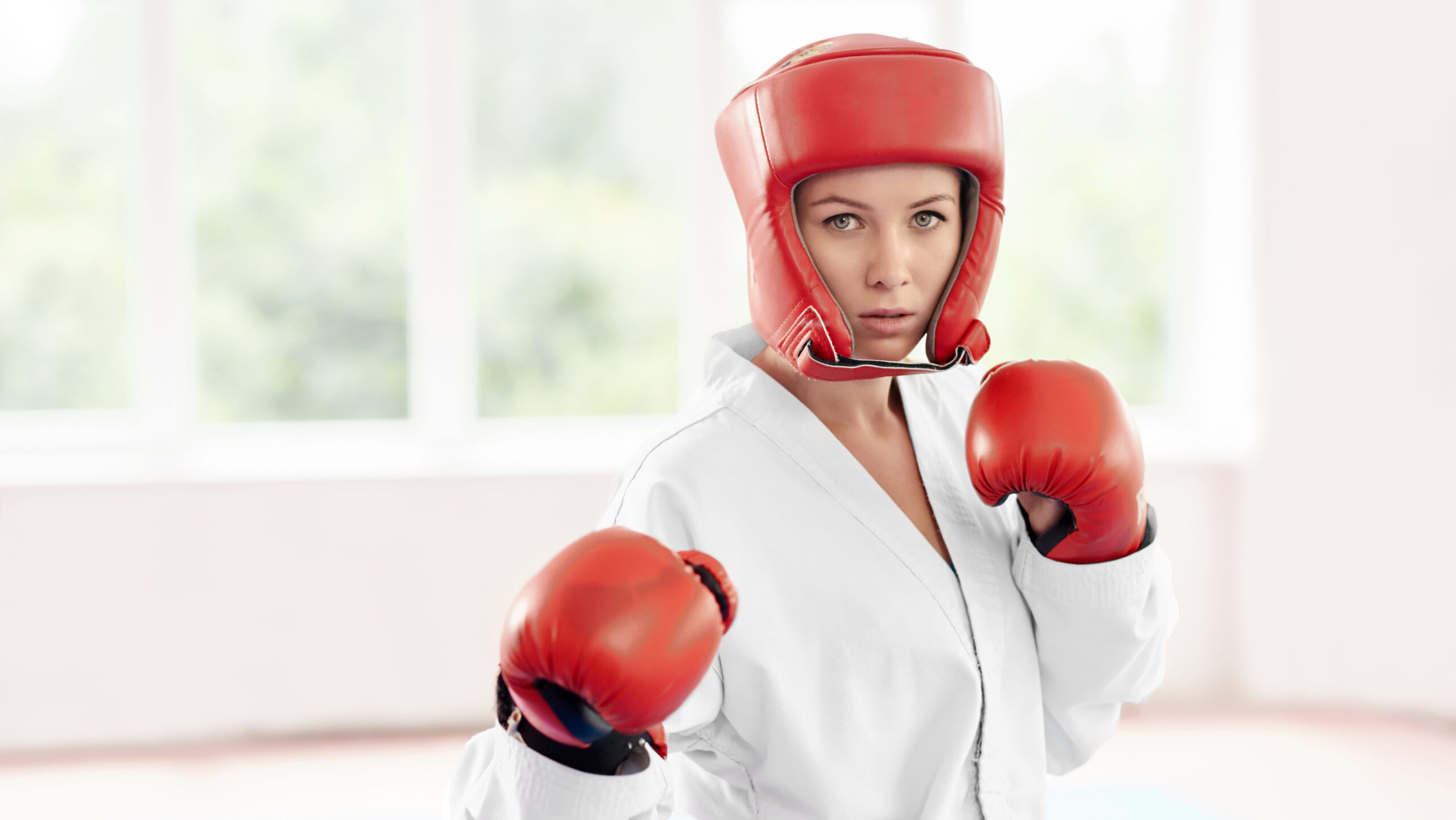 Mulher boxeadora com capacete vermelho e luvas de boxe, pronta para combate na academia de luta, demonstrando força e determinação.