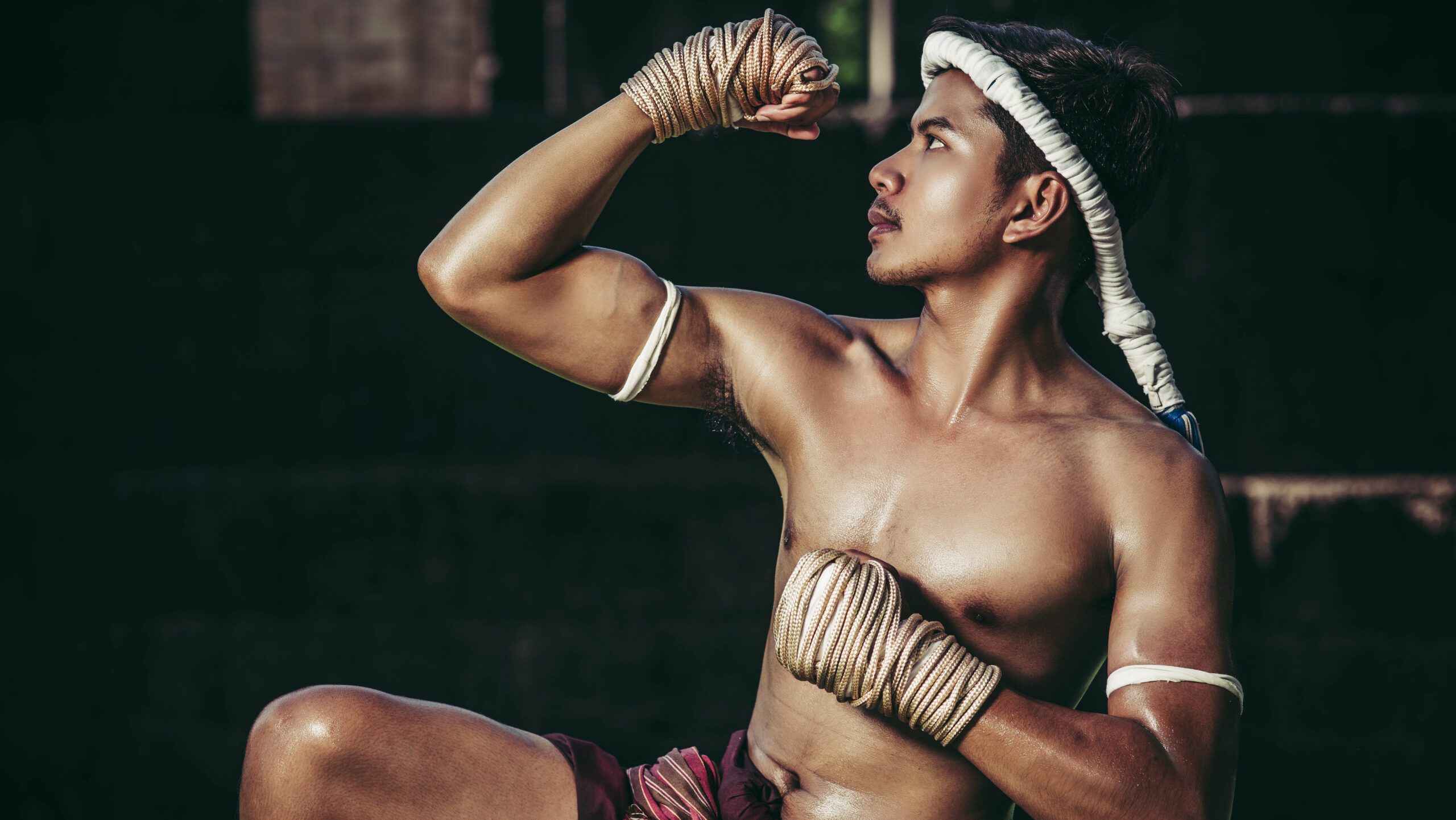 Jovem lutador de muay thai em posição de defesa, vestindo avental provocando uma pose de força e determinação no treinamento de artes marciais.