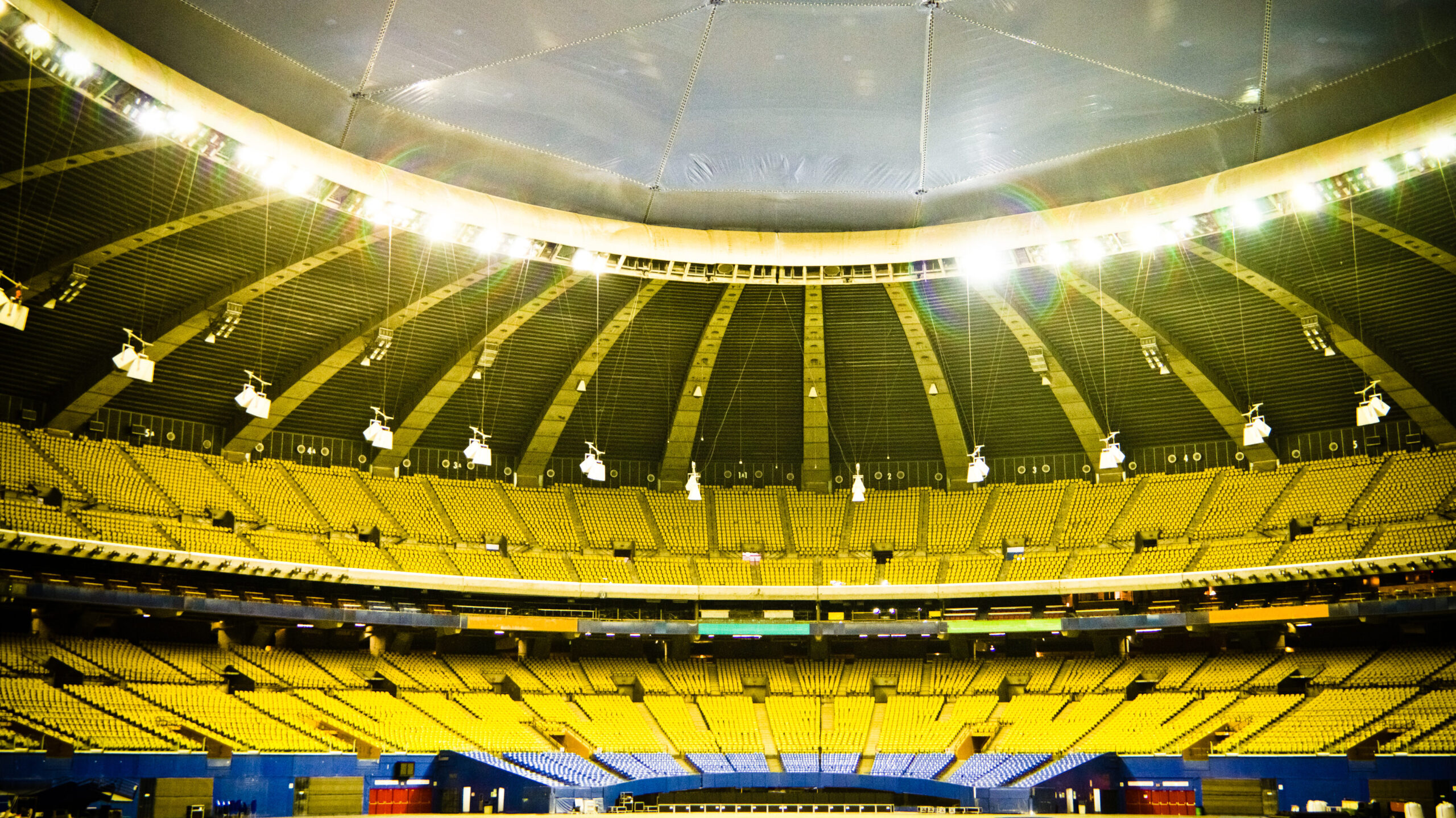 Imagem de um estádio com arquibancadas amarelas e cobertura superior, preparado para uma competição esportiva de grande porte.