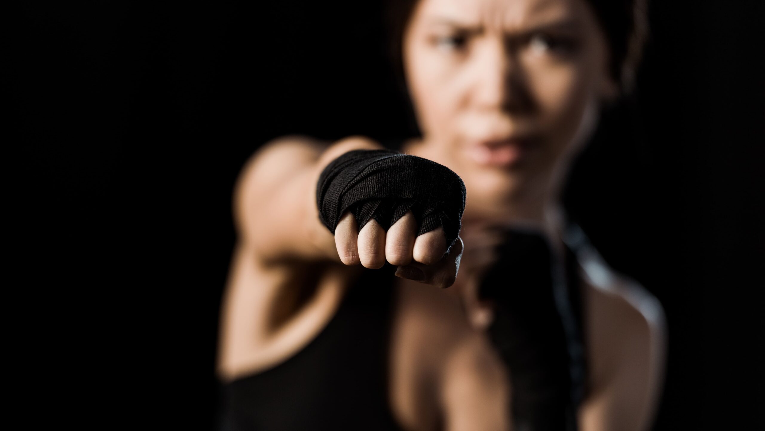 Mulher lutadora em postura de combate, com expressão de determinação, usando roupa esportiva preta e punho em posição de ataque.
