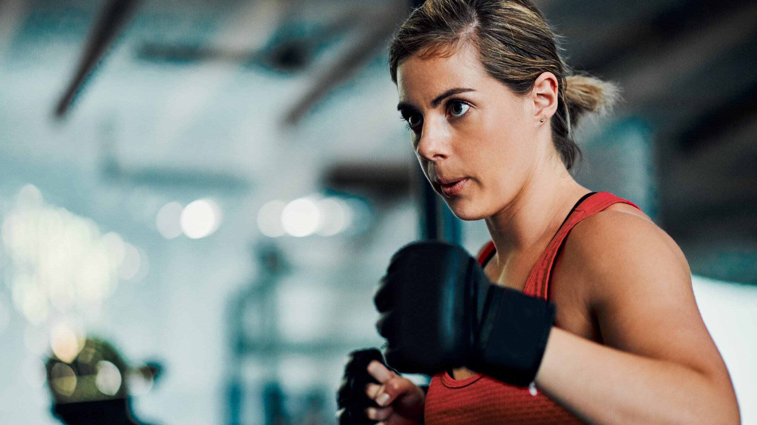 Mulher boxeadora treinando na academia, concentrada e pronta para a luta, com foco na atividade de boxe e preparo físico.