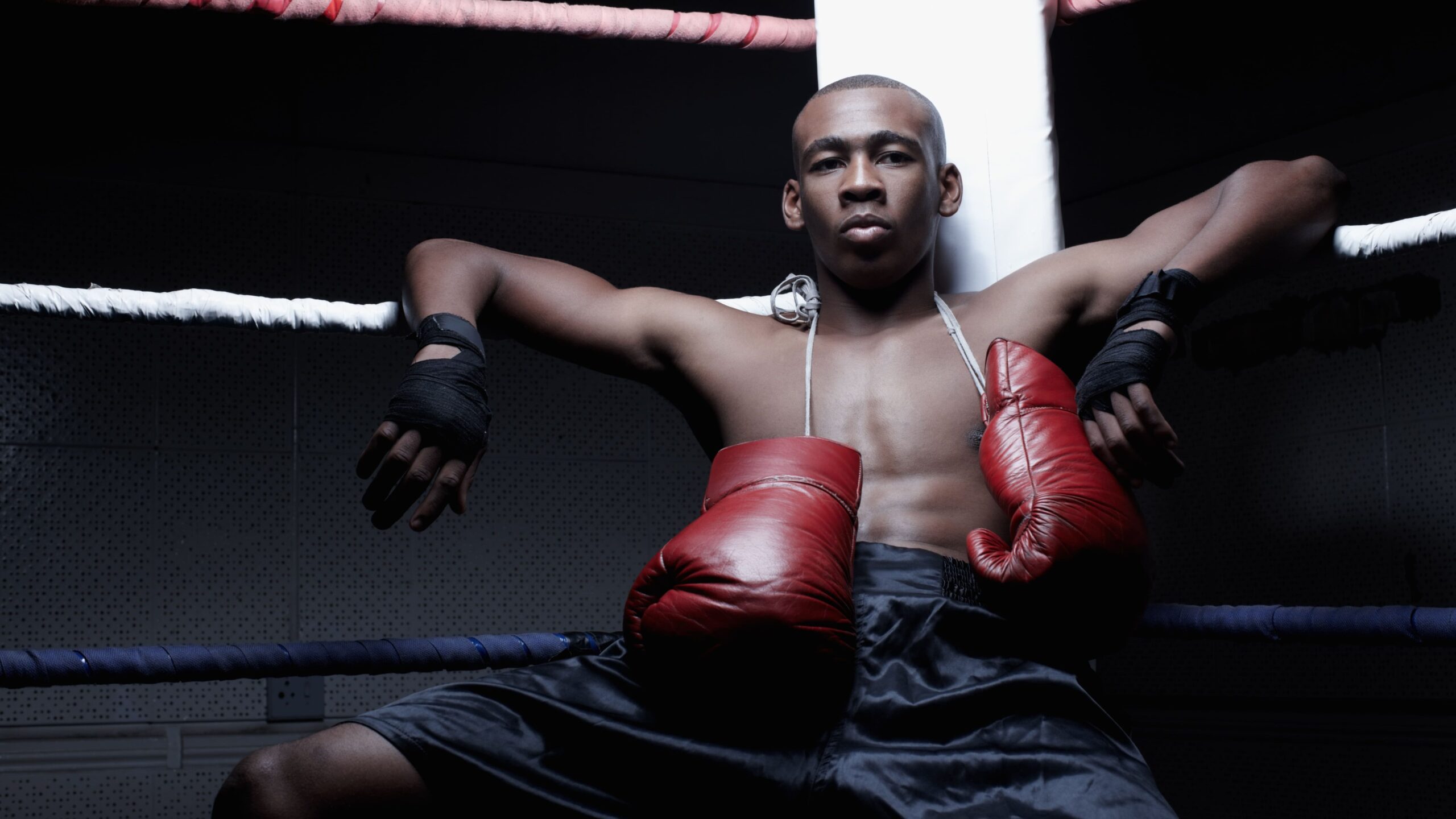 Jovem boxeador dentro do ringue de boxe, usando luvas vermelhas e shorts esportivos, mostrando determinação e força em treino ou competição.