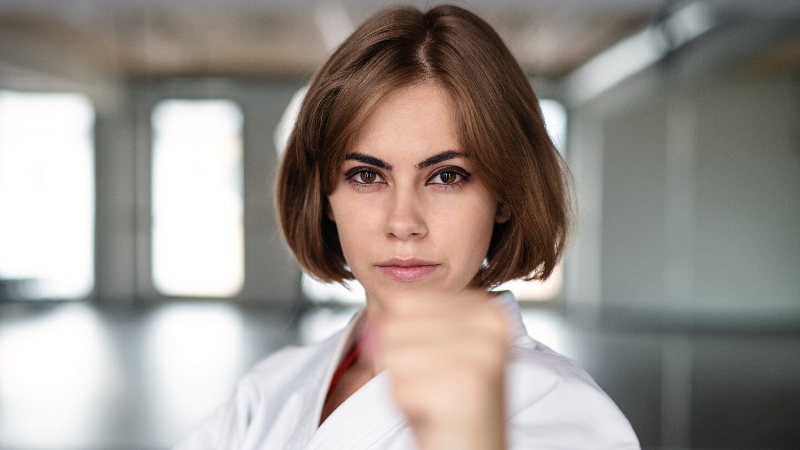 Mulher treinando luta em ambiente moderno e bem iluminado, demonstrando força e determinação com combate de artes marciais.