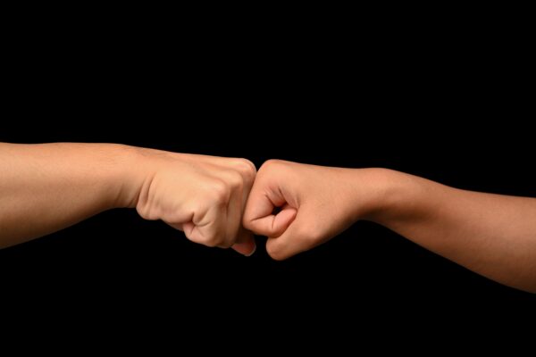 Duas mãos em destaque, com punhos fechados e braços estendidos de um lado a outro, sugerindo desafio ou competição, em fundo preto neutro