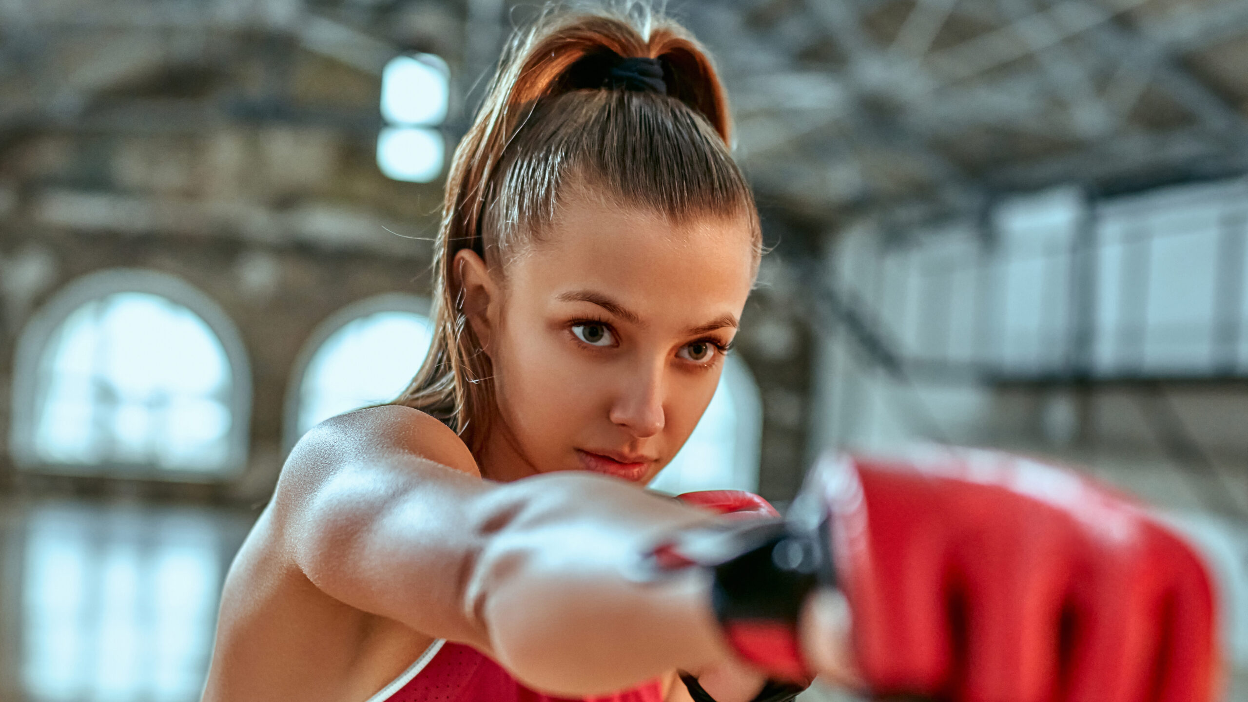 Mulher em academia na posição de ataque com luva vermelha