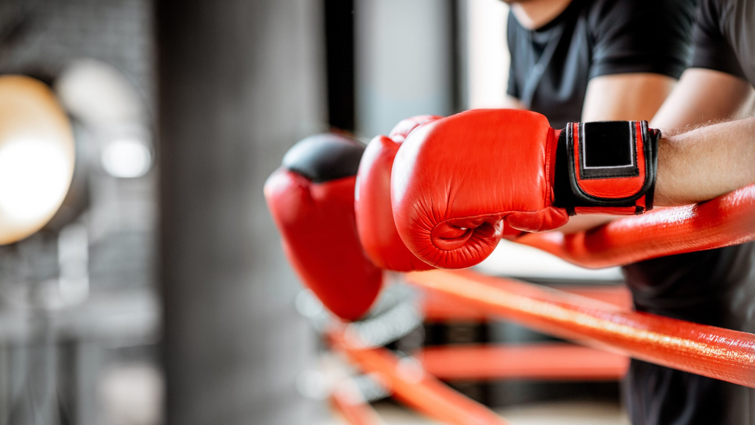 Atleta treinando boxe em uma academia, com luvas vermelhas e faixas no punho. A pessoa segura equipamentos de treino com postura de combate.