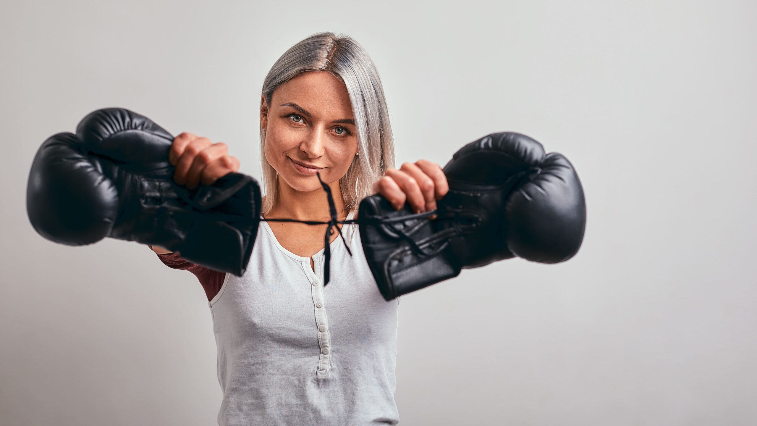 Mulher de cabelo claro segurando à frente do corpo um par de luvas de boxe pretas amarradas pelos cadarços.