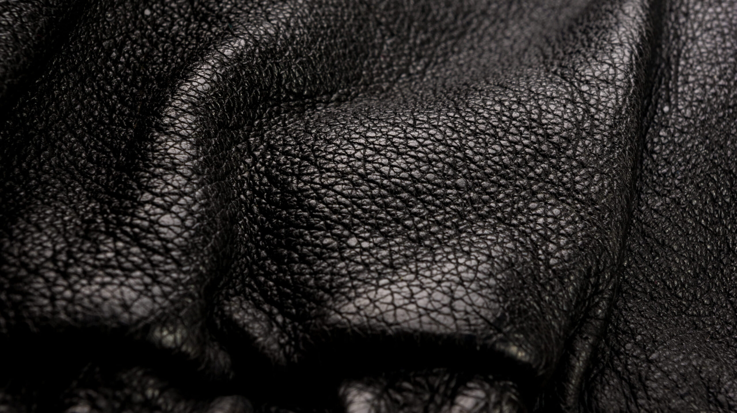 Textura em close-up de material sintético ou couro preto dobrado, destacando os poros e relevos do tecido.
