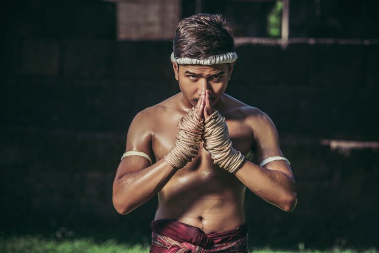Lutador de Muay Thai fazendo saudação tradicional com as mãos juntas em respeito, vestindo mongkhon na cabeça e bandagens de corda estilo Muay Boran.