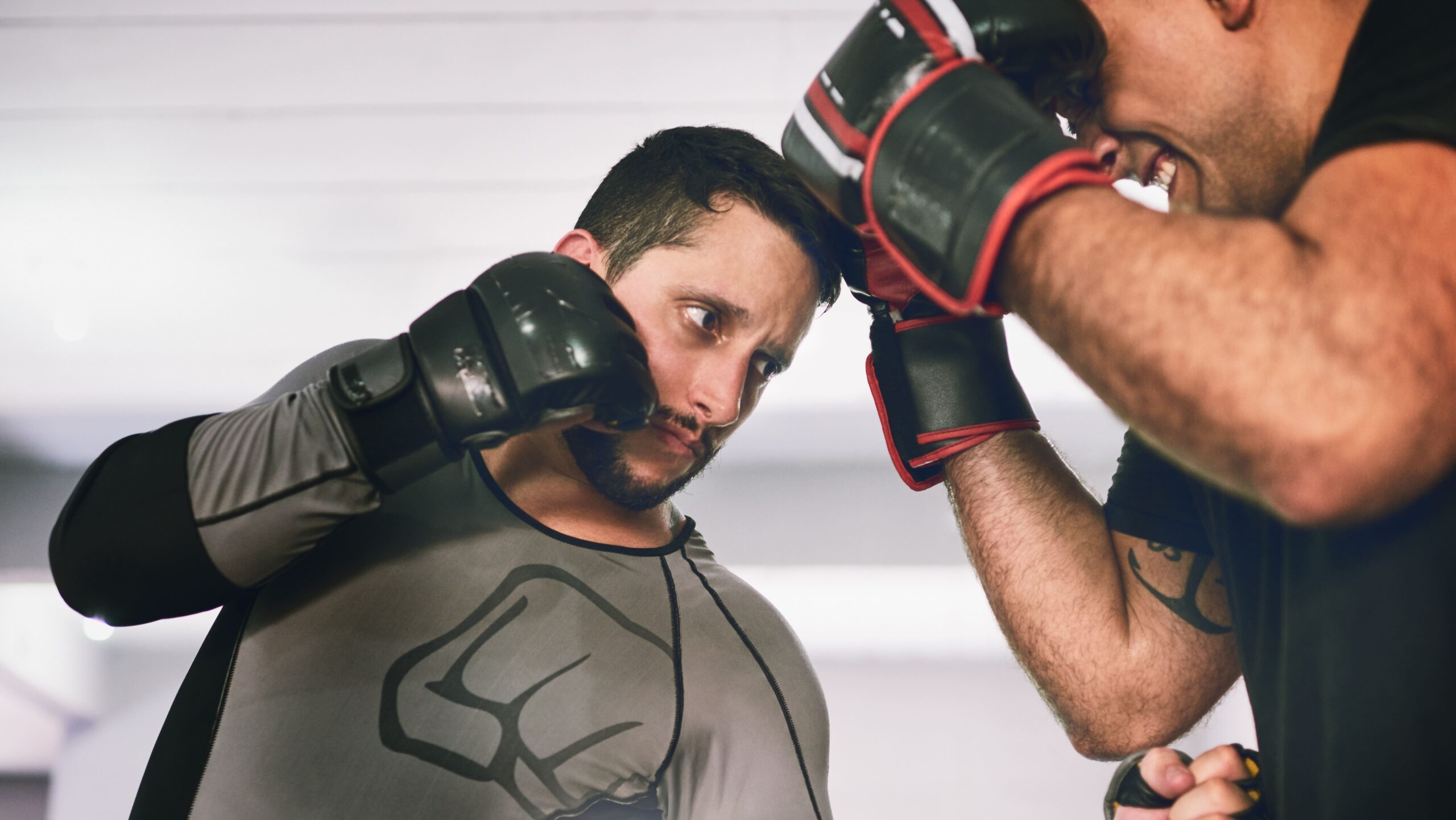 Dois homens treinando boxe em uma academia, com capacetes e luvas, um golpeando e o outro se protegendo durante uma luta