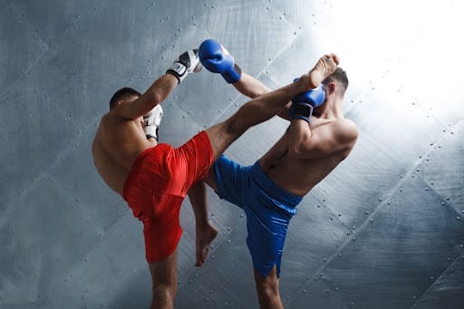 Dois atletas em combate de muay thai no ringue, com um golpe de curta distância e destaque para os movimentos de ataque e defesa no esporte